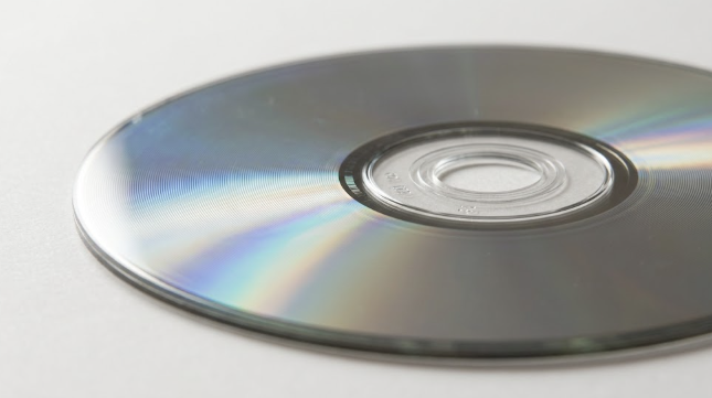 Primer plano de la cara de lectura de un disco optico apoyado sobre una superficie clara, con el anillo interior visible y sin etiqueta ni impresion alguna.